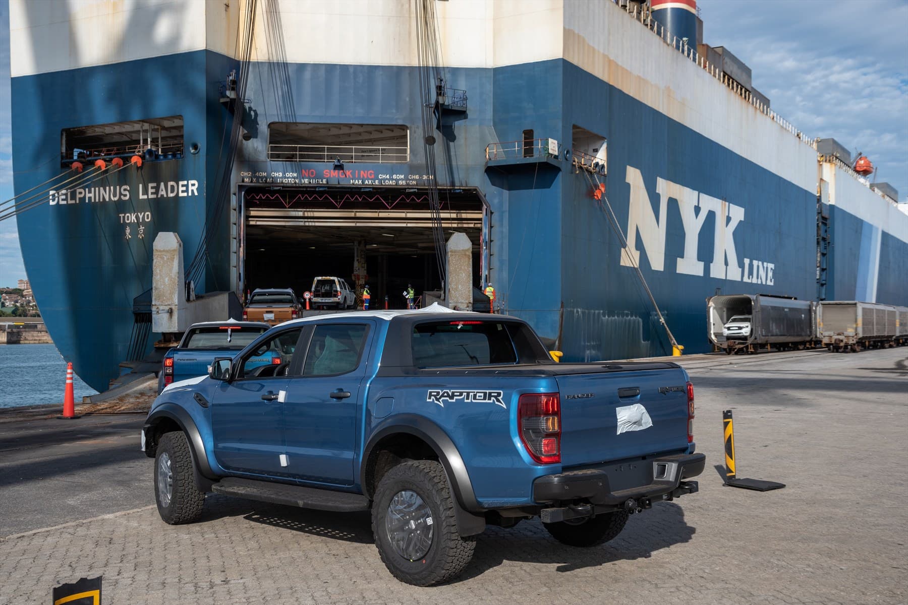 Blue Ford Ranger Raptor truck parked at a port beside a large NYK Line ship.